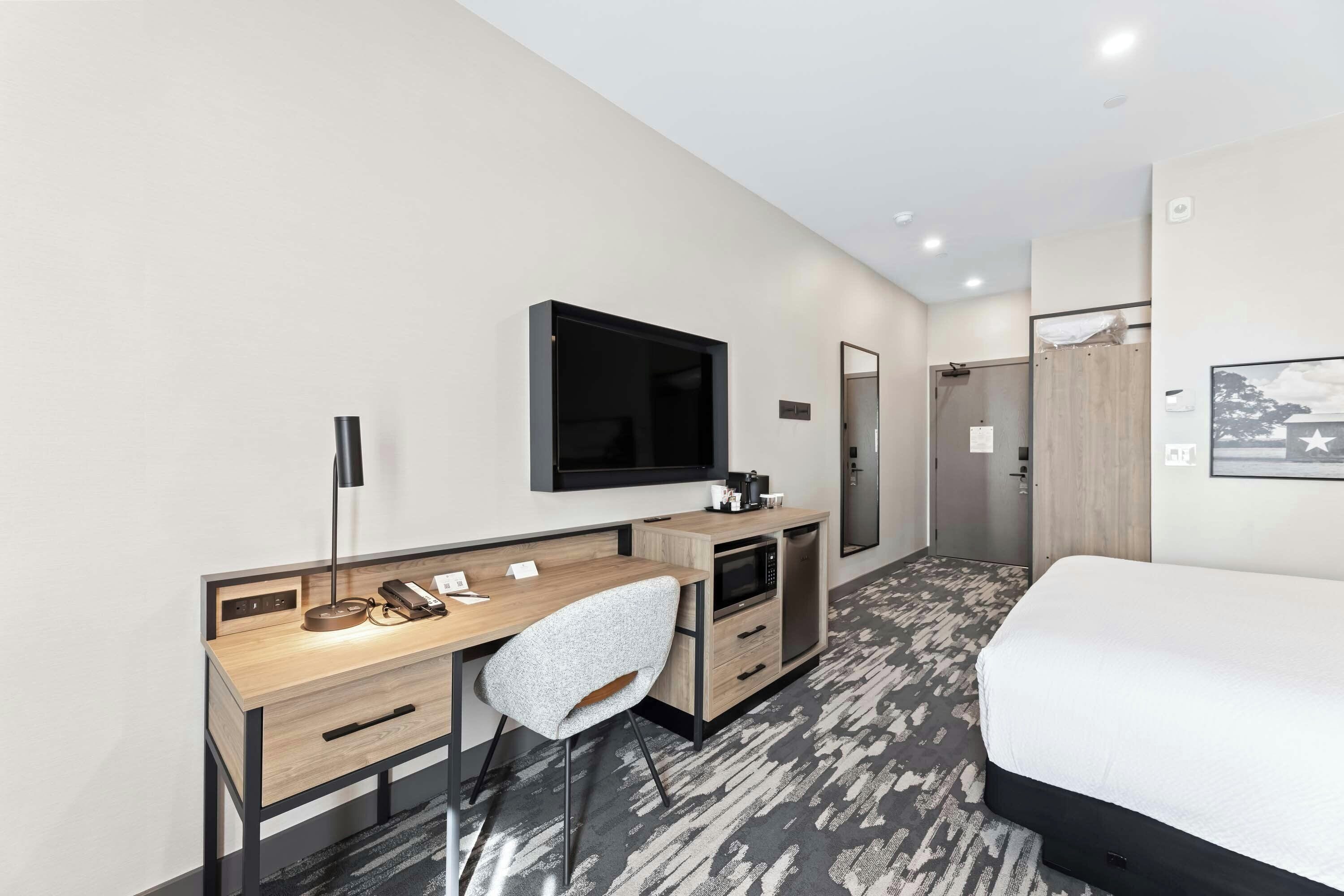 Une chambre d’hôtel comprenant un lit, un bureau avec une chaise, une télévision, un four à micro-ondes et une armoire.