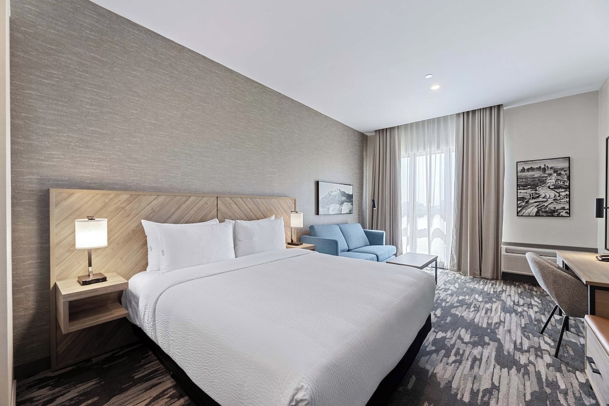 A hotel room with a large bed, a desk, a chair, and a sofa.