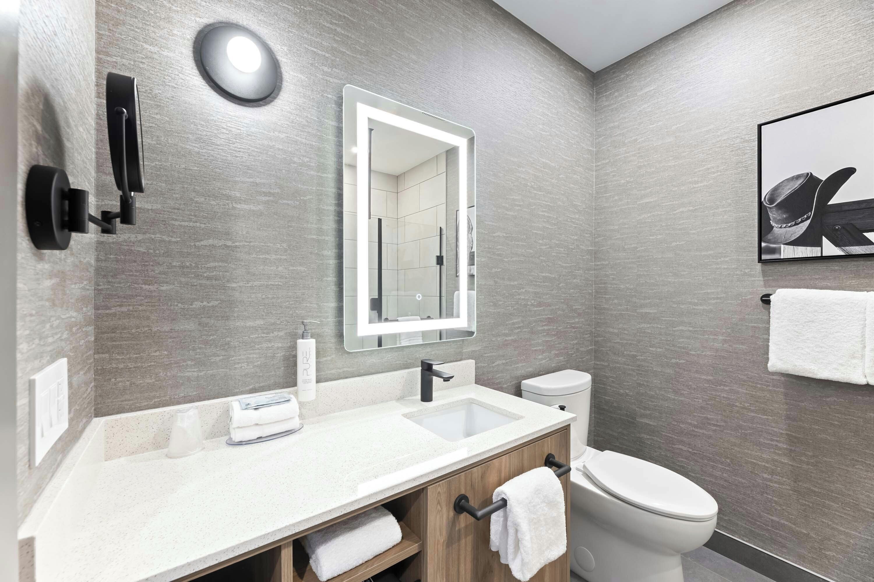 A modern bathroom with a white sink, a mirror, a toilet, and a towel rack.