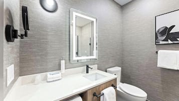 A modern bathroom with a white sink, a mirror, a toilet, and a towel rack.