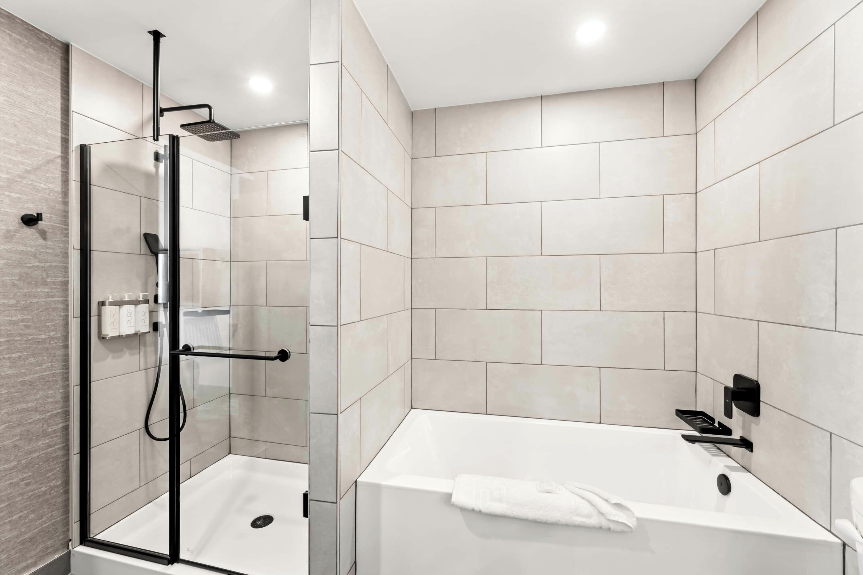 A modern bathroom with a glass-enclosed shower, a white bathtub, and a tiled wall.