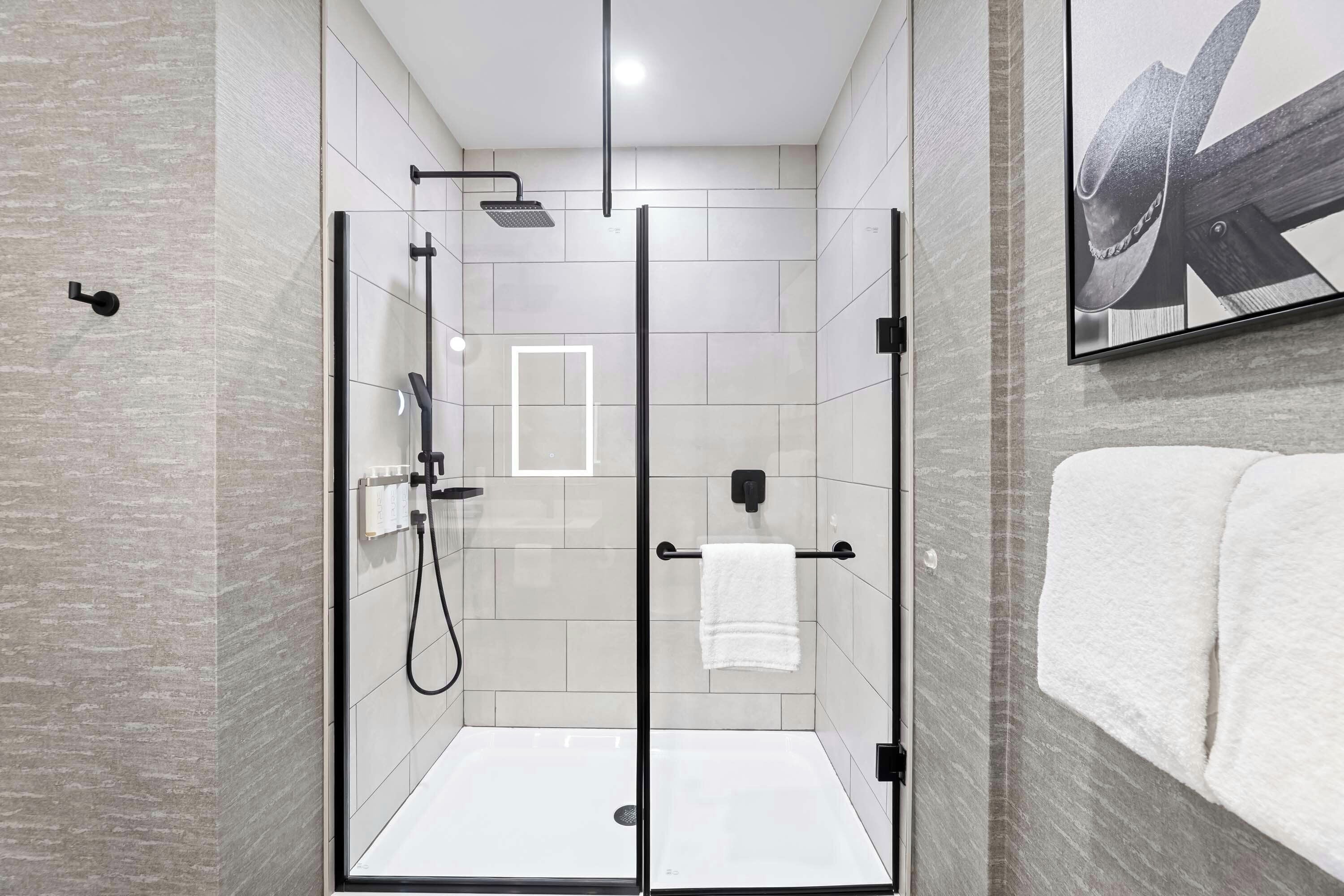A modern bathroom with a glass-enclosed shower, a towel rack, and a framed artwork on the wall.
