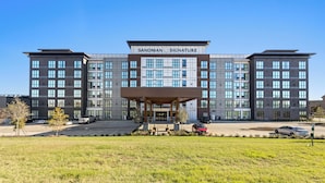 A modern hotel with a prominent entrance and a covered area in front. - Sandman Signature Dallas Las Colinas Hotel & Suites (Irving)