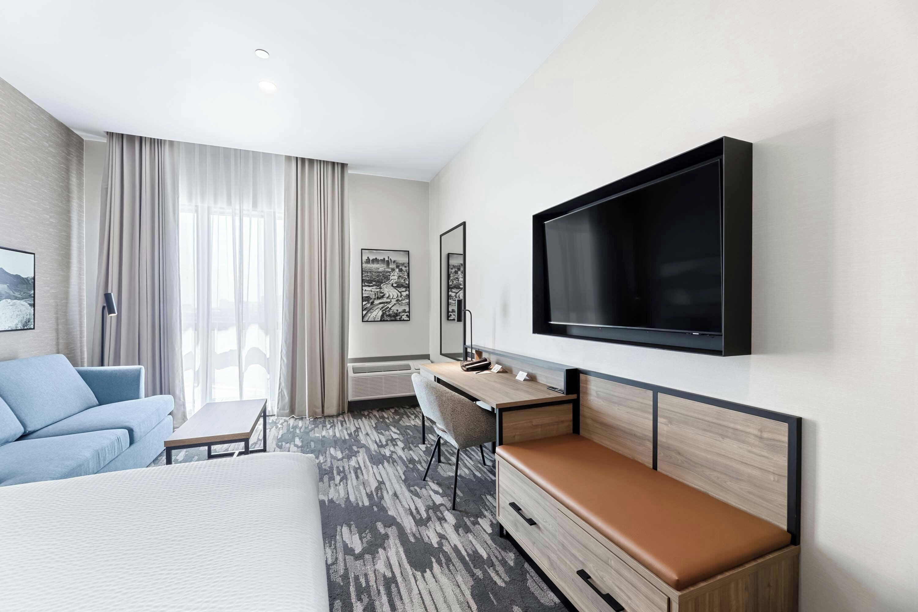 Une chambre d’hôtel moderne équipée d’un lit, d’un bureau, d’une télévision et d’une grande fenêtre avec des rideaux.