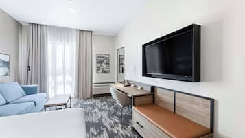 Une chambre d’hôtel moderne équipée d’un lit, d’un bureau, d’une télévision et d’une grande fenêtre avec des rideaux.