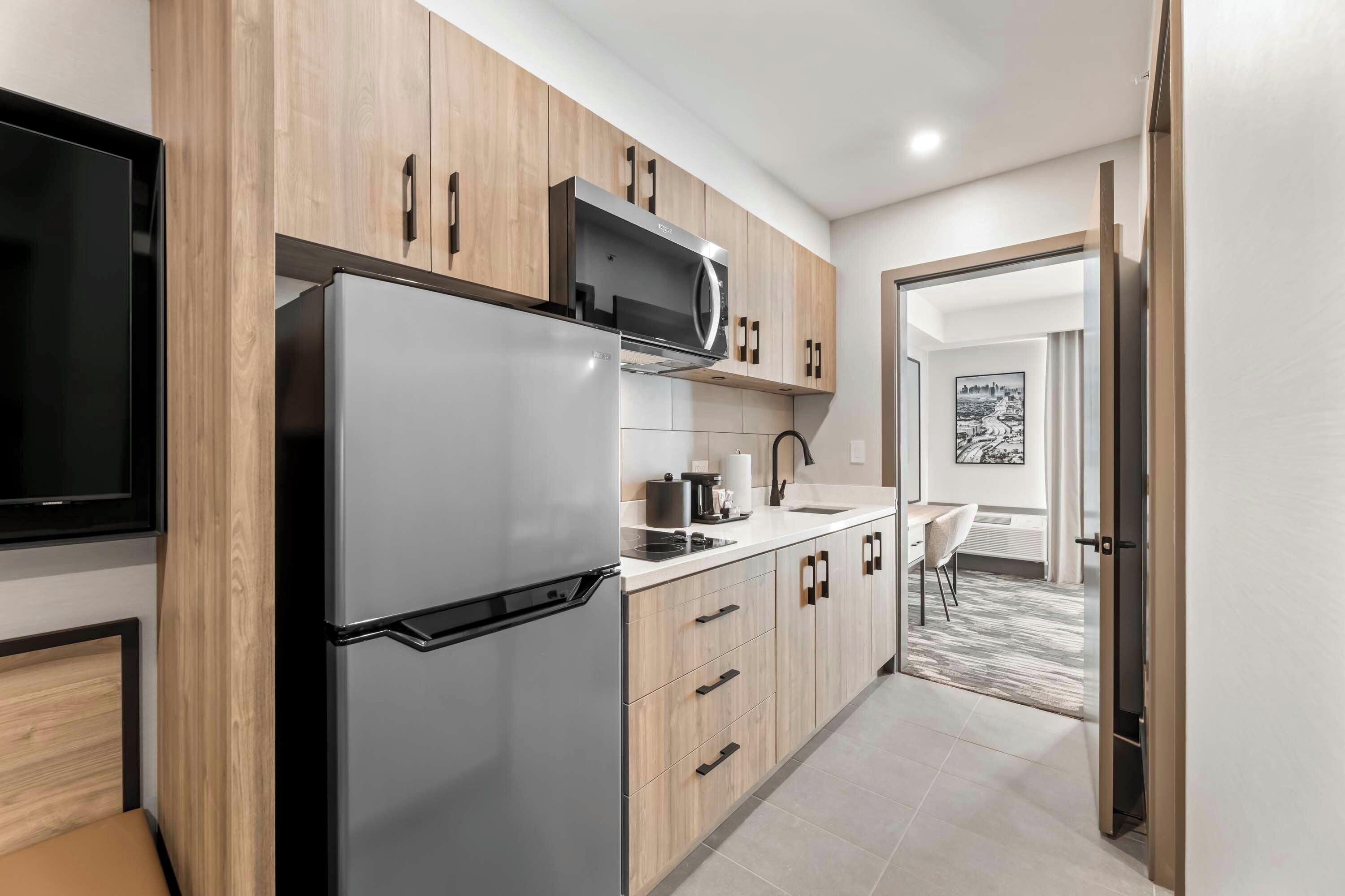 A modern kitchen with a built-in refrigerator, microwave, and stove, wooden cabinets, and a flat-screen TV.