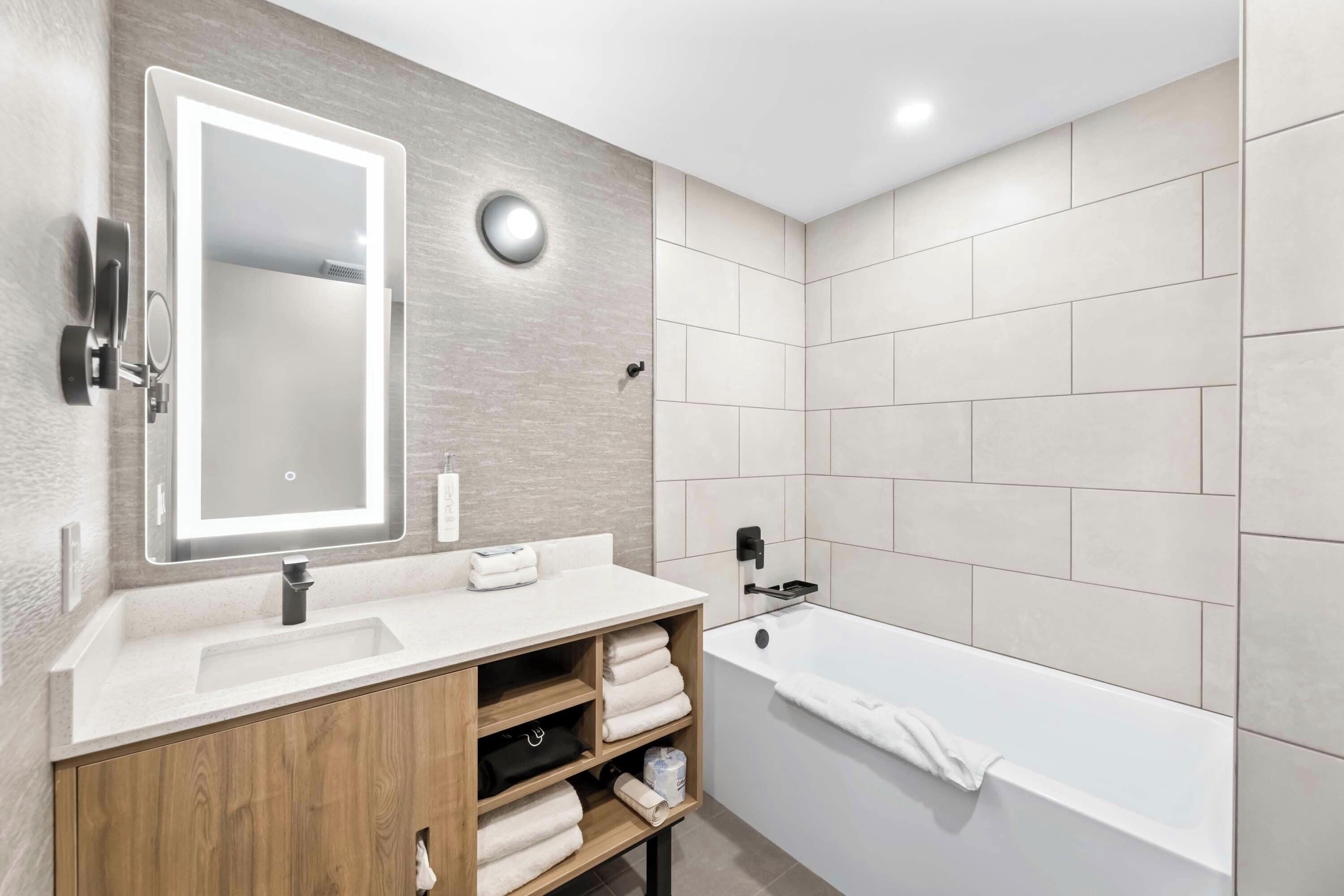 Un baño moderno con un tocador de madera, un espejo grande, una bañera y un perchero para toallas.