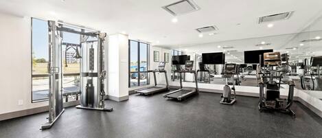 Un gimnasio moderno con diversos equipos de ejercicio, amplias ventanas y un diseño espacioso.