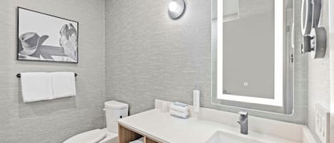 Une salle de bain moderne avec des toilettes, un lavabo et un miroir. Un tableau encadré est accroché au mur, et il y a un porte-serviettes.