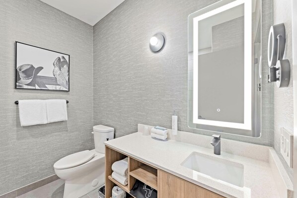 A modern bathroom with a toilet, sink, and mirror. There is a framed picture on the wall and a towel rack.