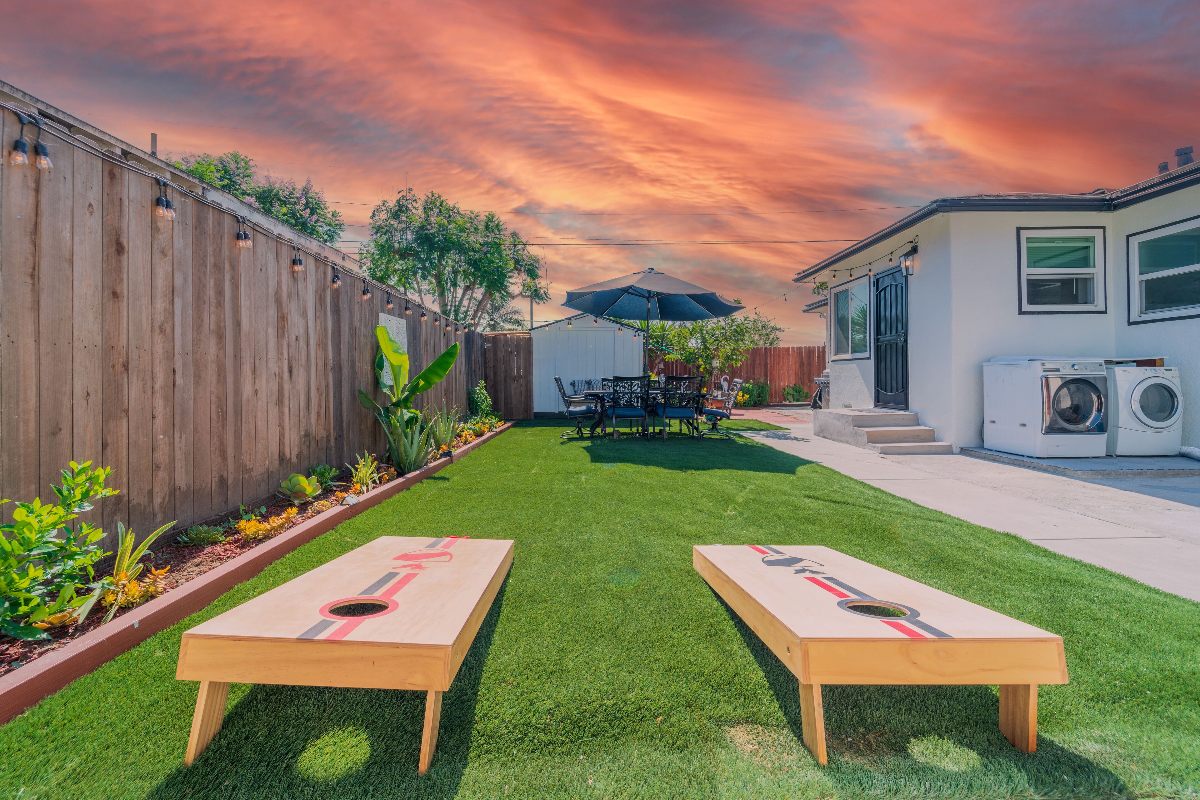 A backyard with two wooden tables, a wooden fence, a washing machine, and a patio umbrella.