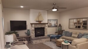 A living room with a fireplace, a ceiling fan, and a television. - Sail Away - Waldport (Waldport)
