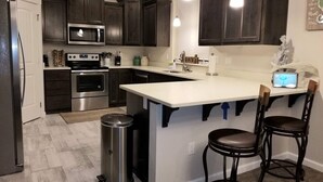 A modern kitchen with dark wood cabinets, stainless steel appliances, a white island with bar stools, and pendant lighting. - Sail Away - Waldport (Waldport)