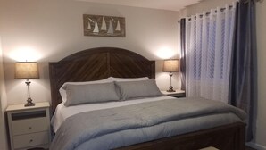 A bedroom with a large bed, two bedside tables, a bench, and a wall-mounted artwork. - Sail Away - Waldport (Waldport)