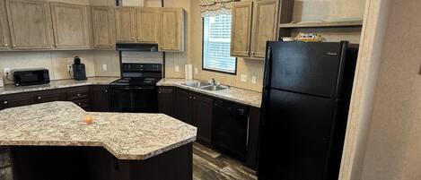 A modern kitchen with dark wood cabinets, a granite countertop, a black refrigerator, and a built-in oven.