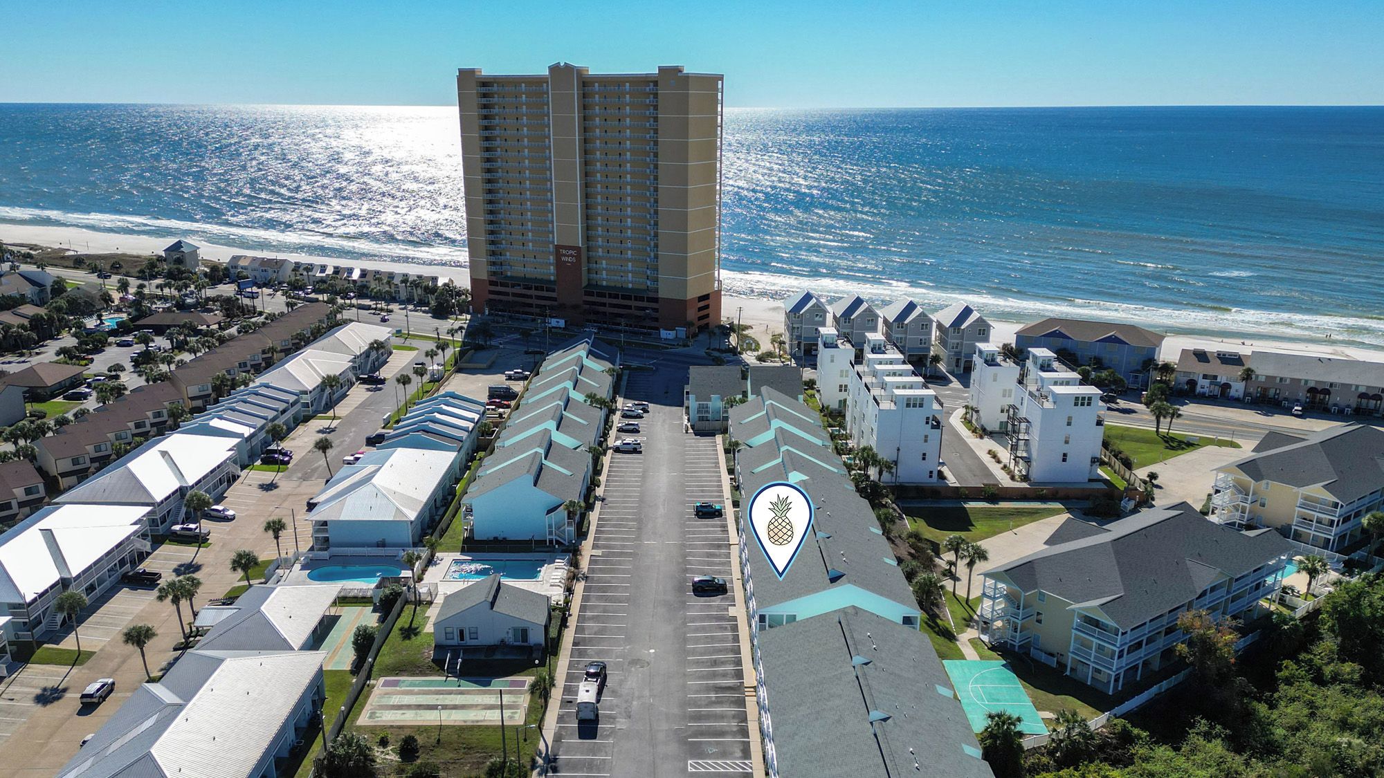 A coastal hotel with multiple-story buildings, a parking lot, and a view of the ocean.