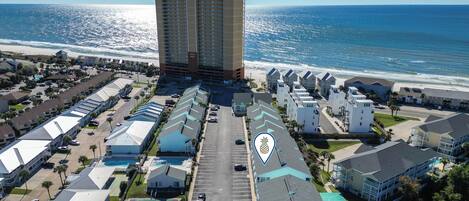 A coastal hotel with multiple-story buildings, a parking lot, and a view of the ocean.