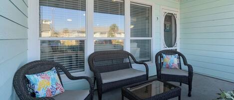 A covered porch with wicker furniture and a glass table.