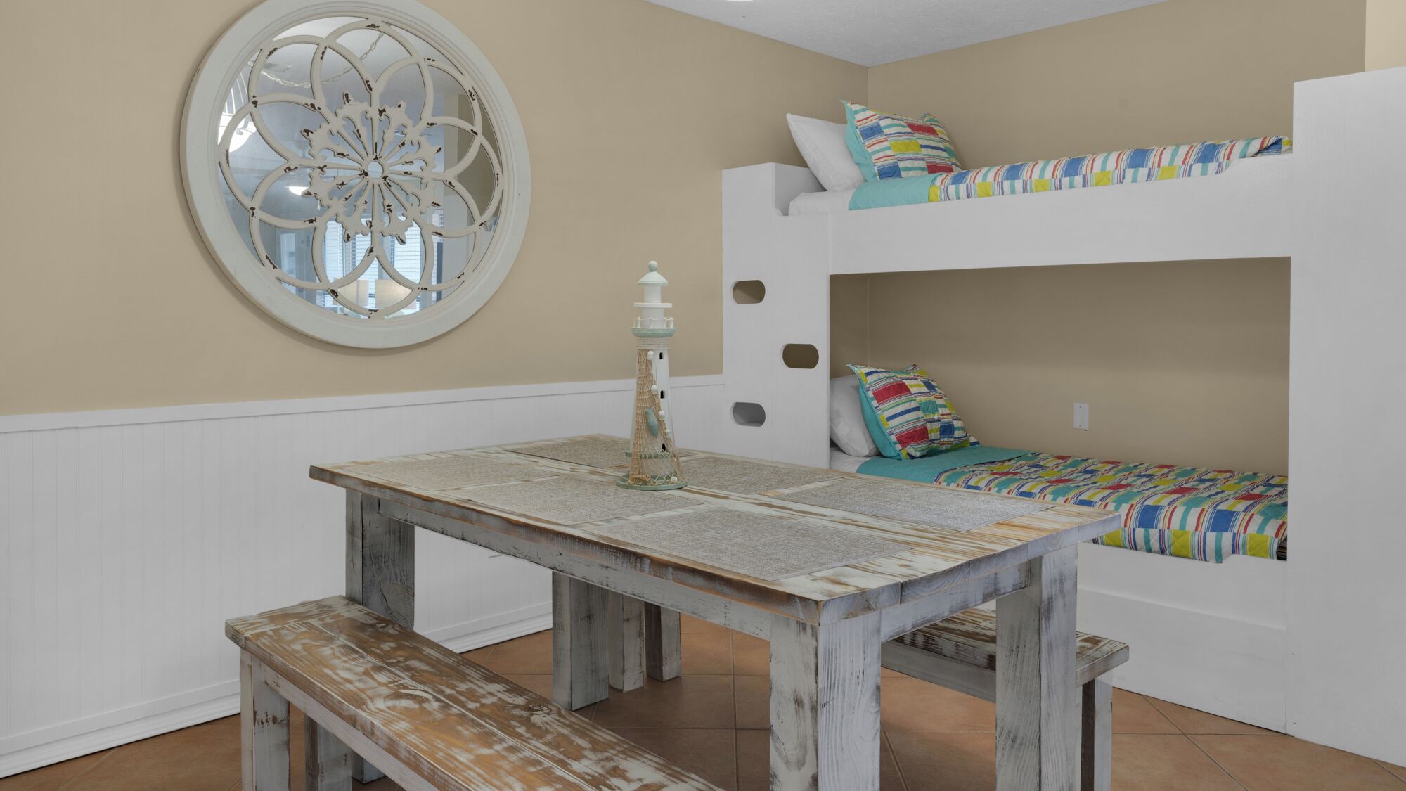 A room with a bunk bed, a round mirror, a wooden table, and a bench.