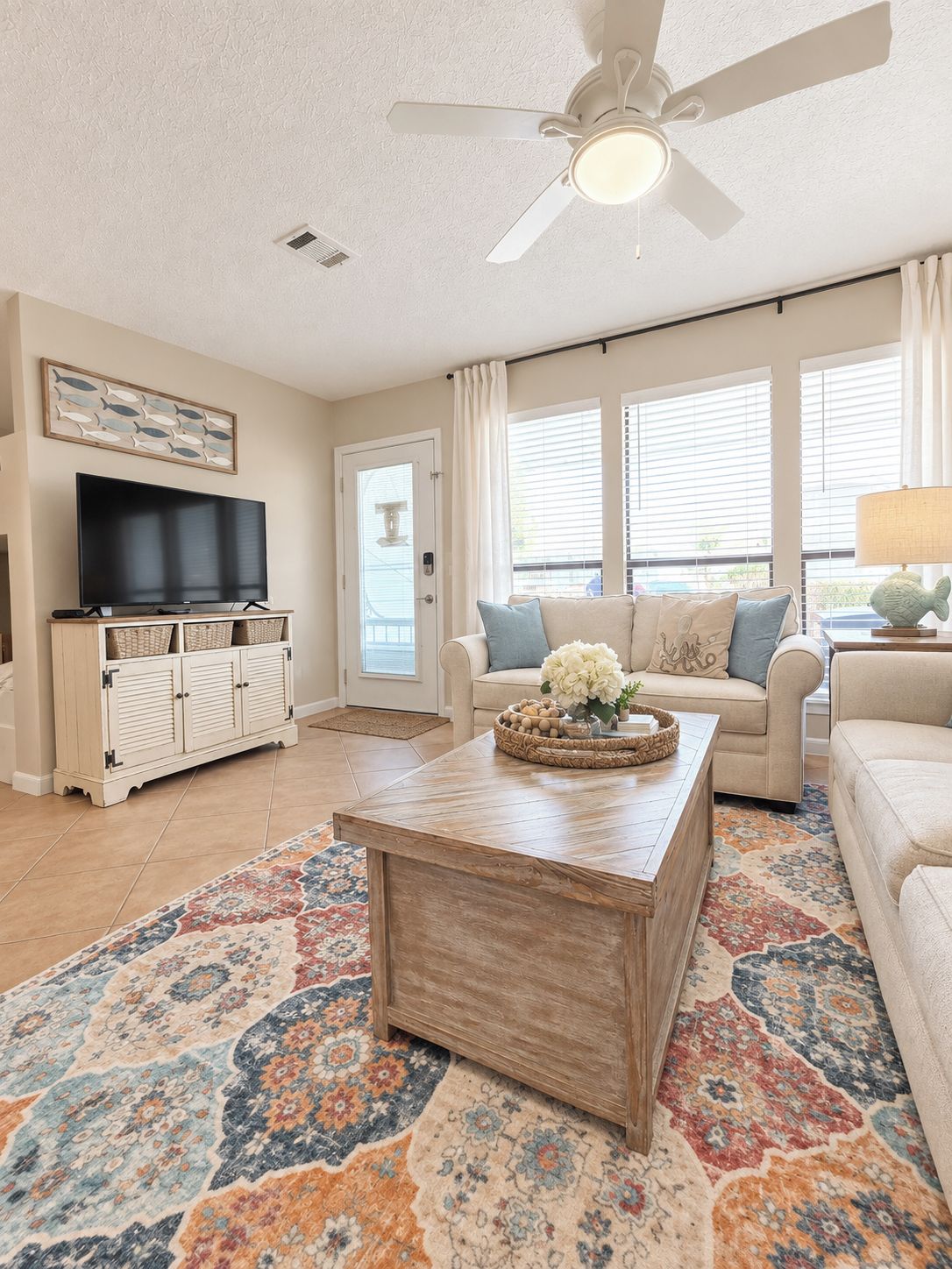 A living room with a ceiling fan, a television, a sofa, a coffee table, and a patterned rug.