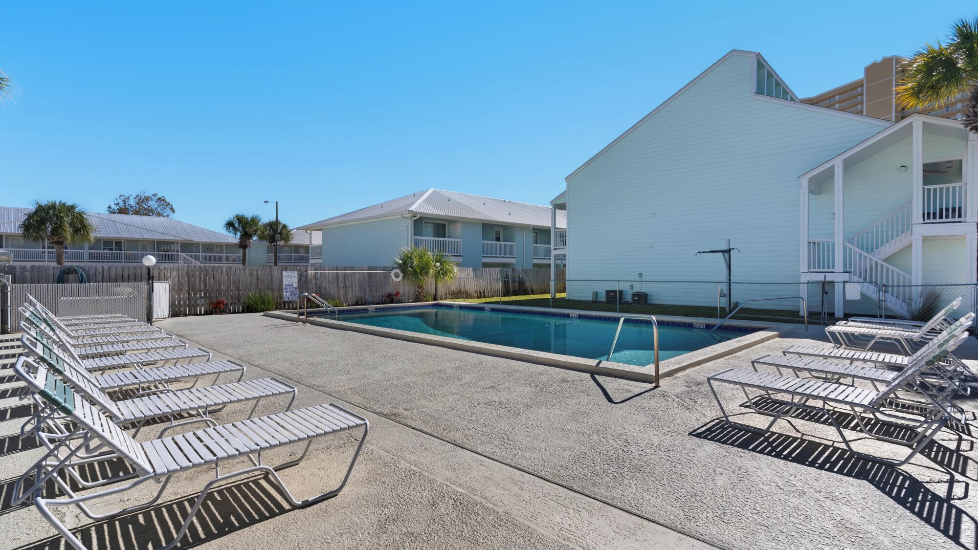 Ein Swimmingpool mit Liegestühlen, ein Holzzaun und ein weißes Gebäude mit Balkonen.