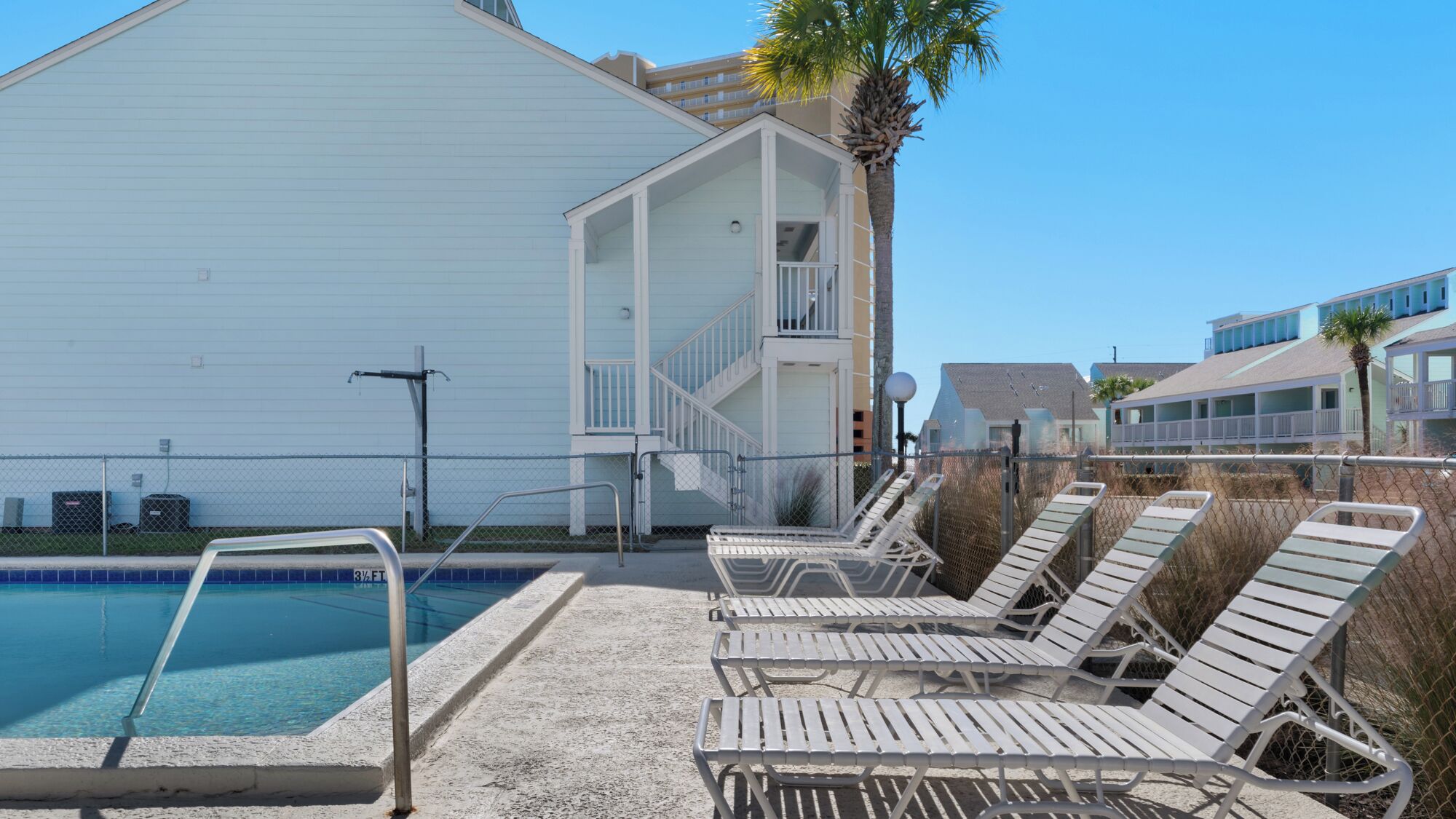 A poolside area with lounge chairs, a pool, and a building with a balcony.