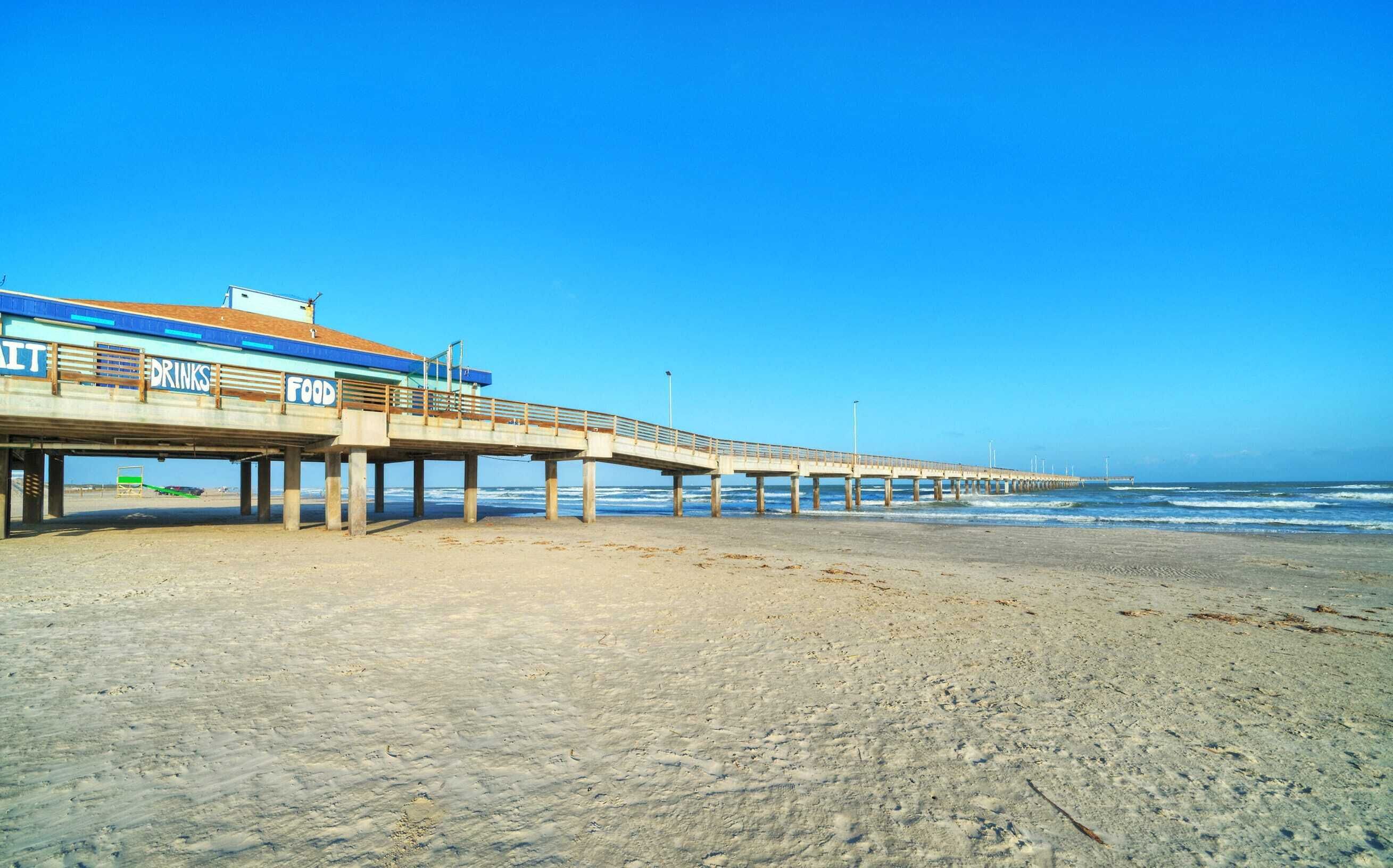 Een steiger met een restaurant genaamd "UNIT DRINKS FOOD" die zich uitstrekt over het strand.