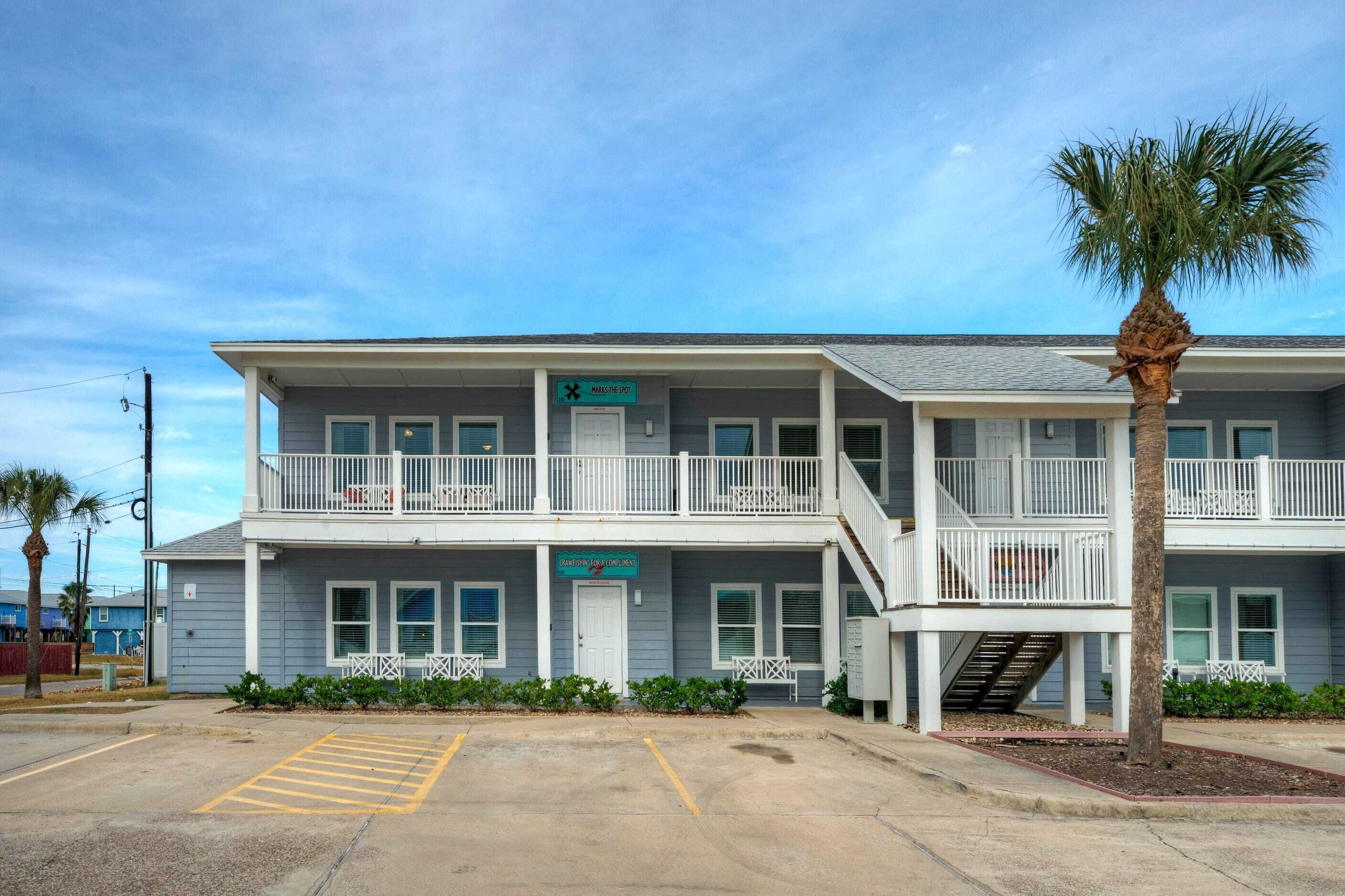 A two-story motel with a balcony on the second floor, a parking lot in front, and a palm tree to the right.