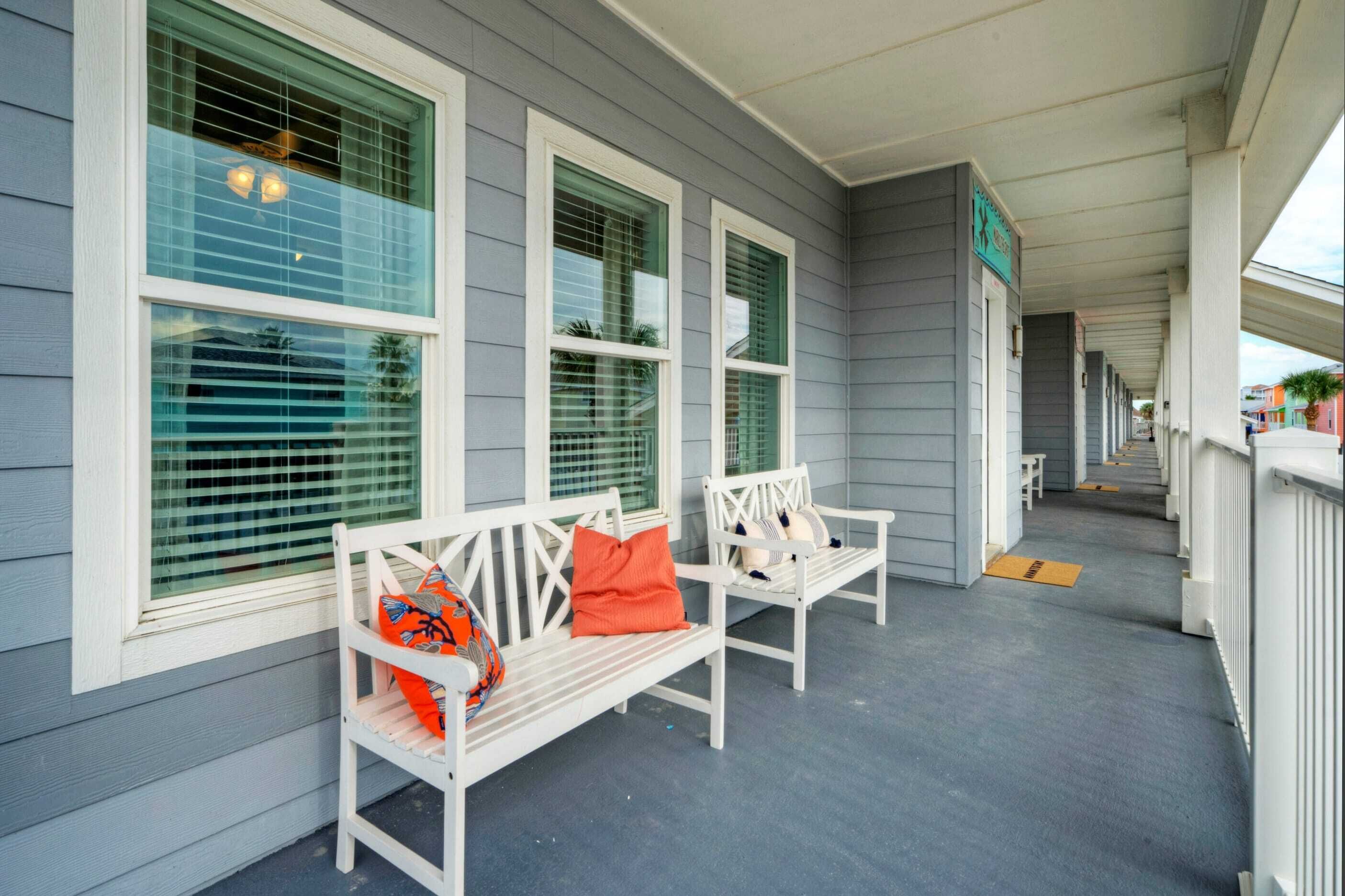 A covered porch with white benches and green window blinds.