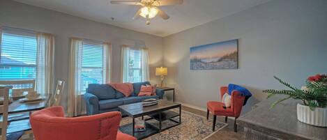 A living room with a sofa, chairs, a coffee table, a lamp, a painting, and a ceiling fan.