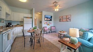 A modern kitchen with white cabinets, a dining area with chairs, a sofa, and a lamp.