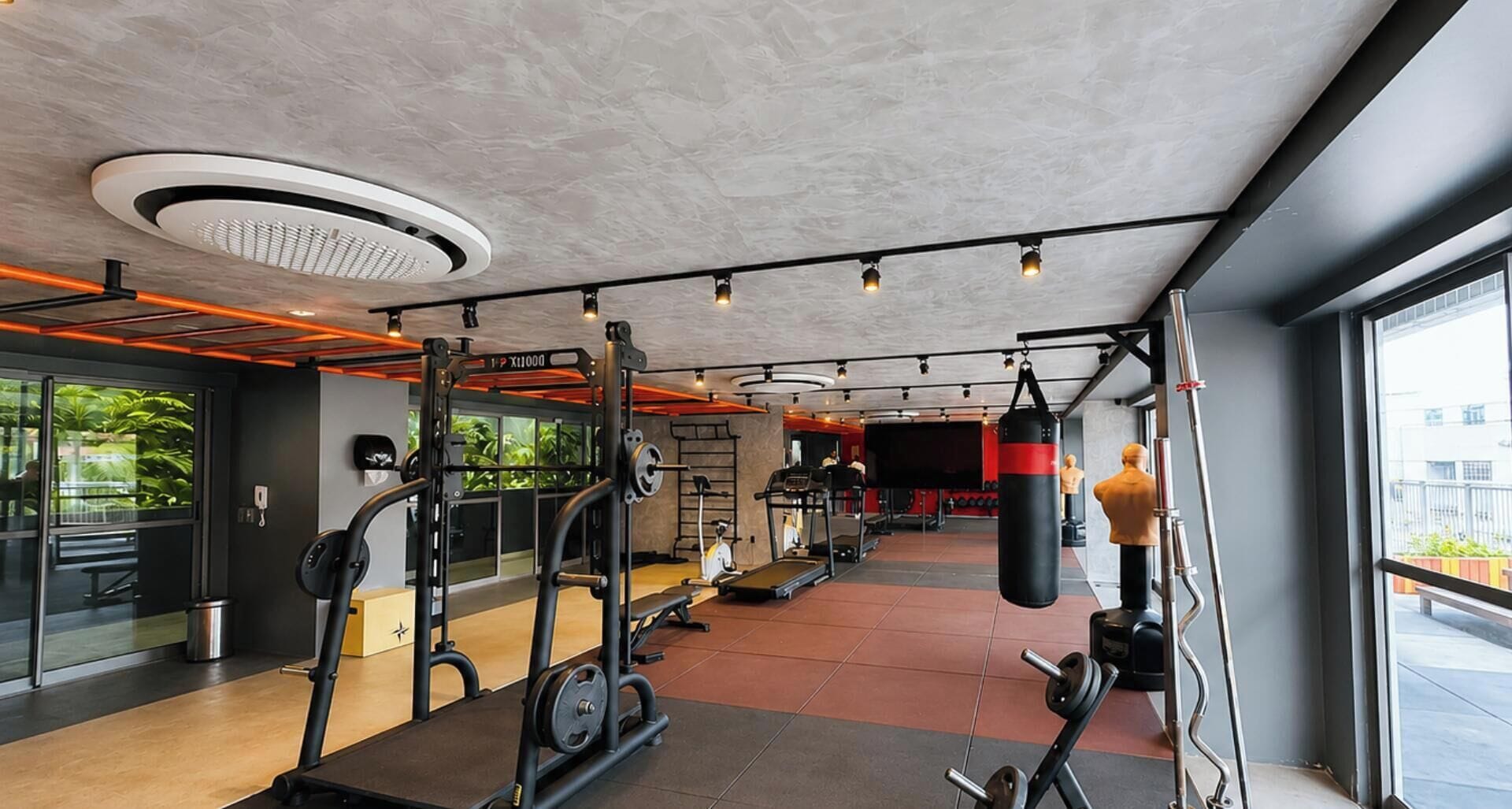 A gym with various exercise equipment, a punching bag, and a view of the outside through large windows.