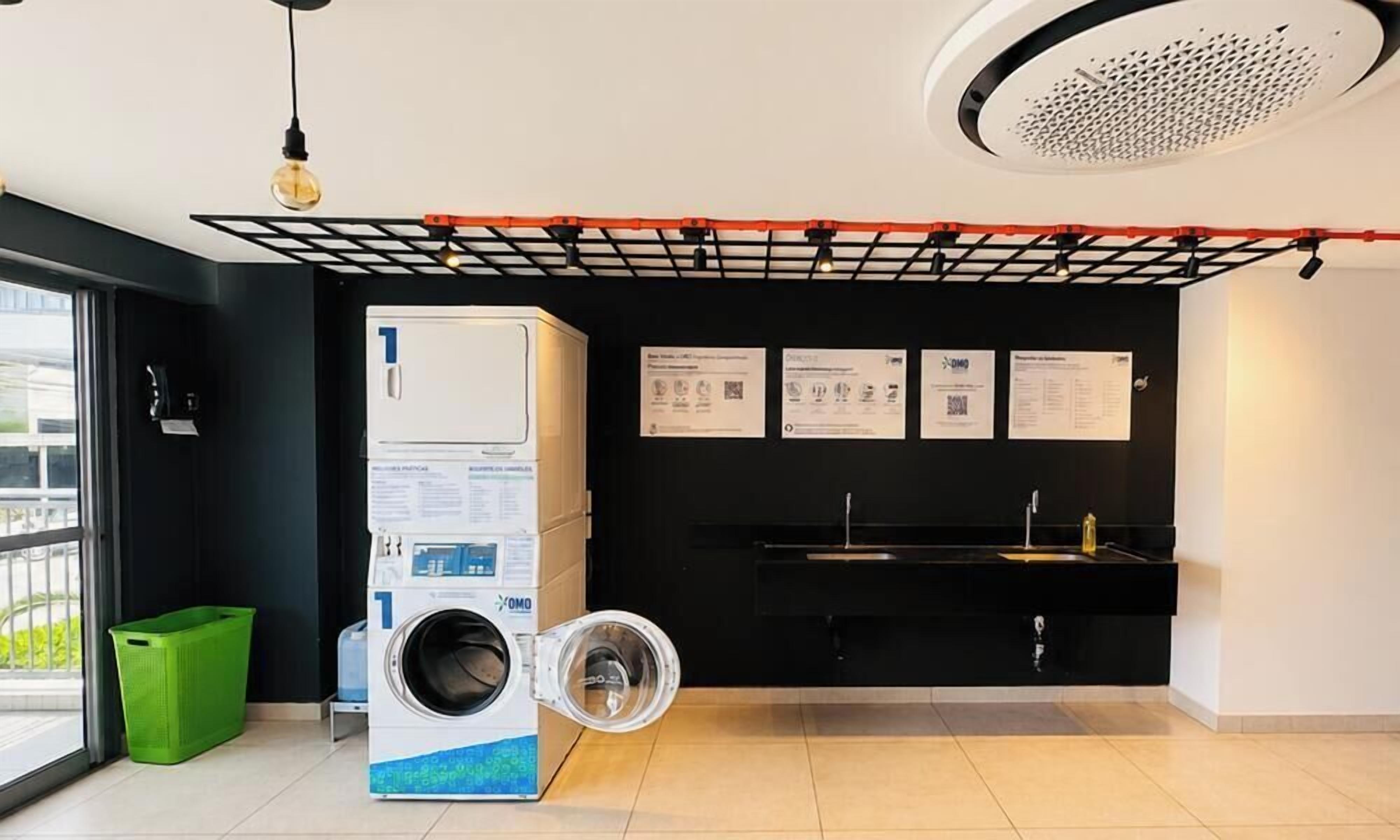A modern laundry room with a front-loading washing machine, a sink, and a black countertop.