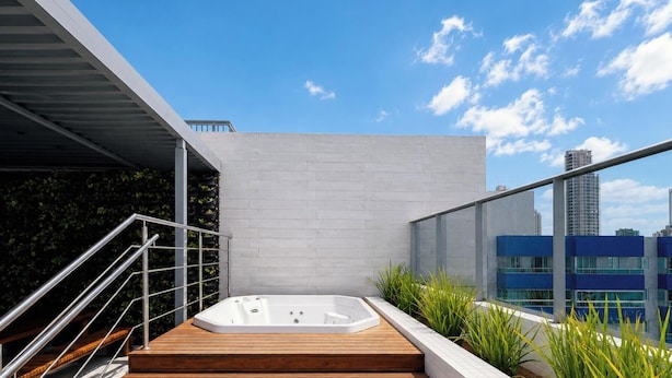 A rooftop terrace with a hot tub, a wooden deck, a metal staircase, and a city skyline view. - Box 150 - LikeHome Hospedagens (João Pessoa)