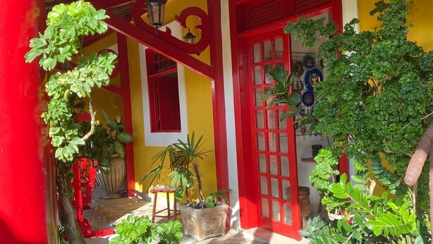 A courtyard with a wooden ceiling, red and yellow walls, and potted plants. - Pousada Leão (Maceio)
