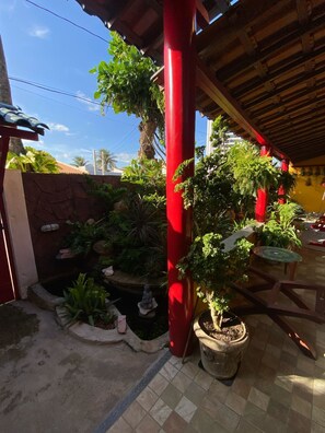 A covered outdoor area with red pillars, potted plants, a small pond, and a tiled floor. - Pousada Leão (Maceio)