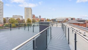 En takterrass med ett glasräcke som erbjuder utsikt över de omgivande byggnaderna och träden.