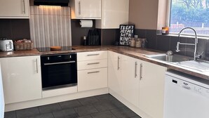 Een moderne keuken met witte kasten, een zwarte afzuigkap, een inbouwoven, een vaatwasser en een raam met uitzicht op bomen.