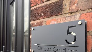 Een huurdersbord met het nummer '5', bevestigd aan een bakstenen muur, met een deur en raam op de achtergrond.