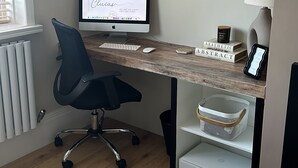Een werkplek aan huis met een bureau, computer, stoel en schappen.