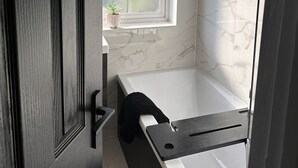 Een moderne badkamer met een badkuip, een raam met een plant en marmeren tegels.