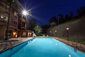A swimming pool with steps and railings, surrounded by a brick wall and a wooden building with balconies.