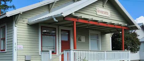 A single-story house with a porch, a red door, and a sign that reads "The WOODSHED."