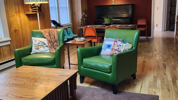 A cozy living room with two green leather armchairs, a wooden coffee table, a television, and a piano.