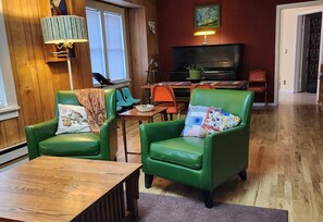 Een gezellige woonkamer met twee groene leren fauteuils, een houten salontafel, een televisie en een piano.