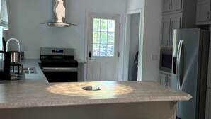 A modern kitchen with a central island, bar stools, stainless steel appliances, and a window with a view.