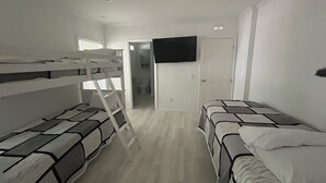 A room with bunk beds, a television mounted on the wall, and a door leading to a bathroom.