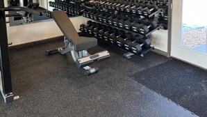 A gym with weightlifting equipment, treadmills, and a mirror reflecting the space.