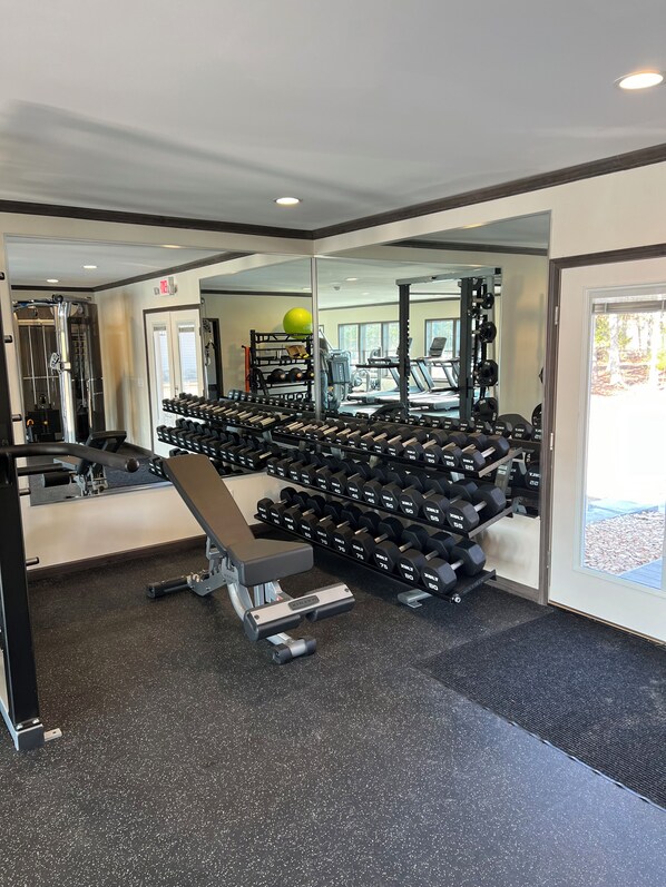 A gym with weightlifting equipment, treadmills, and a mirror reflecting the space.
