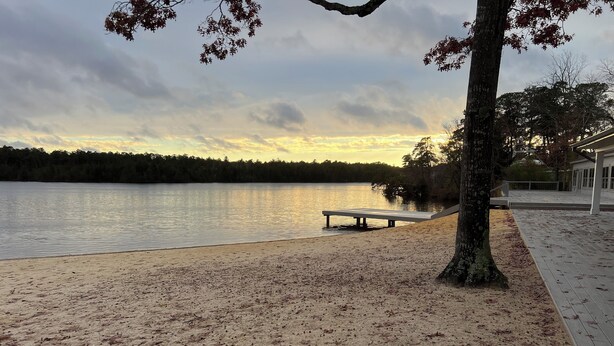 A lakeside walkway with a bench, trees, and a wooden deck.